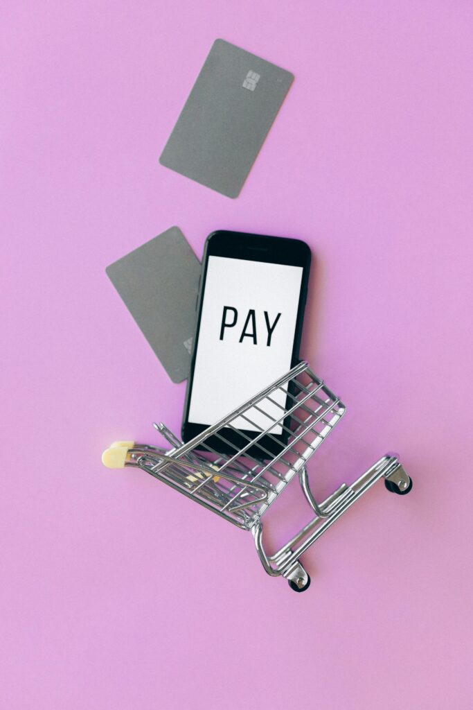 Top view of a smartphone in a shopping cart with credit cards on a purple background.